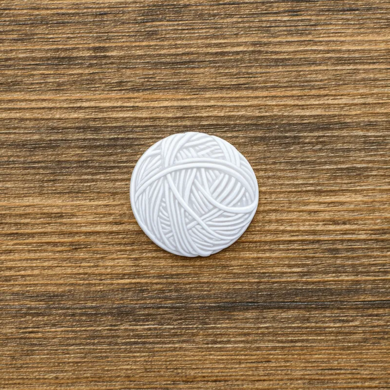 Miniature Masterpiece - A tiny, perfectly shaped 3D printed sticker of a yarn ball, with an emphasis on texture and detail, captured in a cozy, artistic setting.